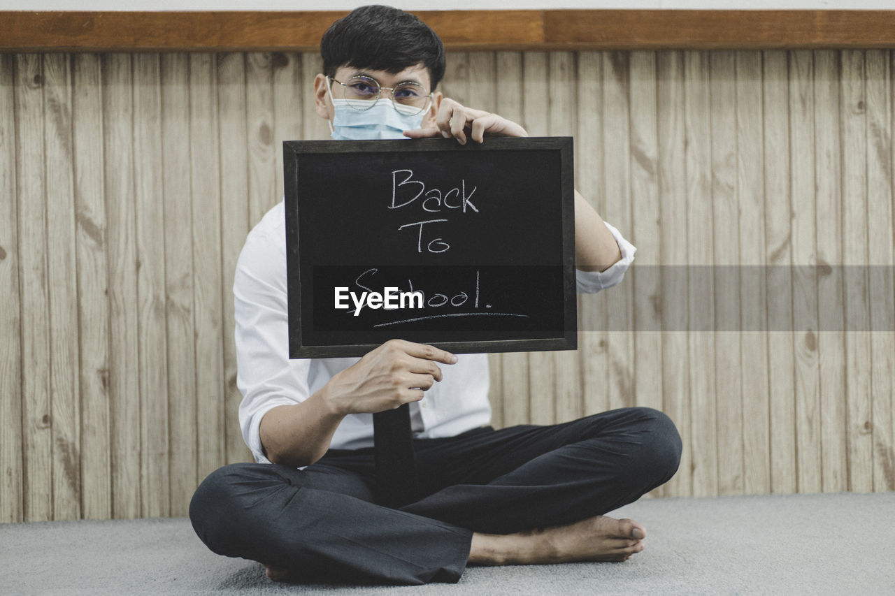 Portrait of man wearing flu mask holding slate against wall