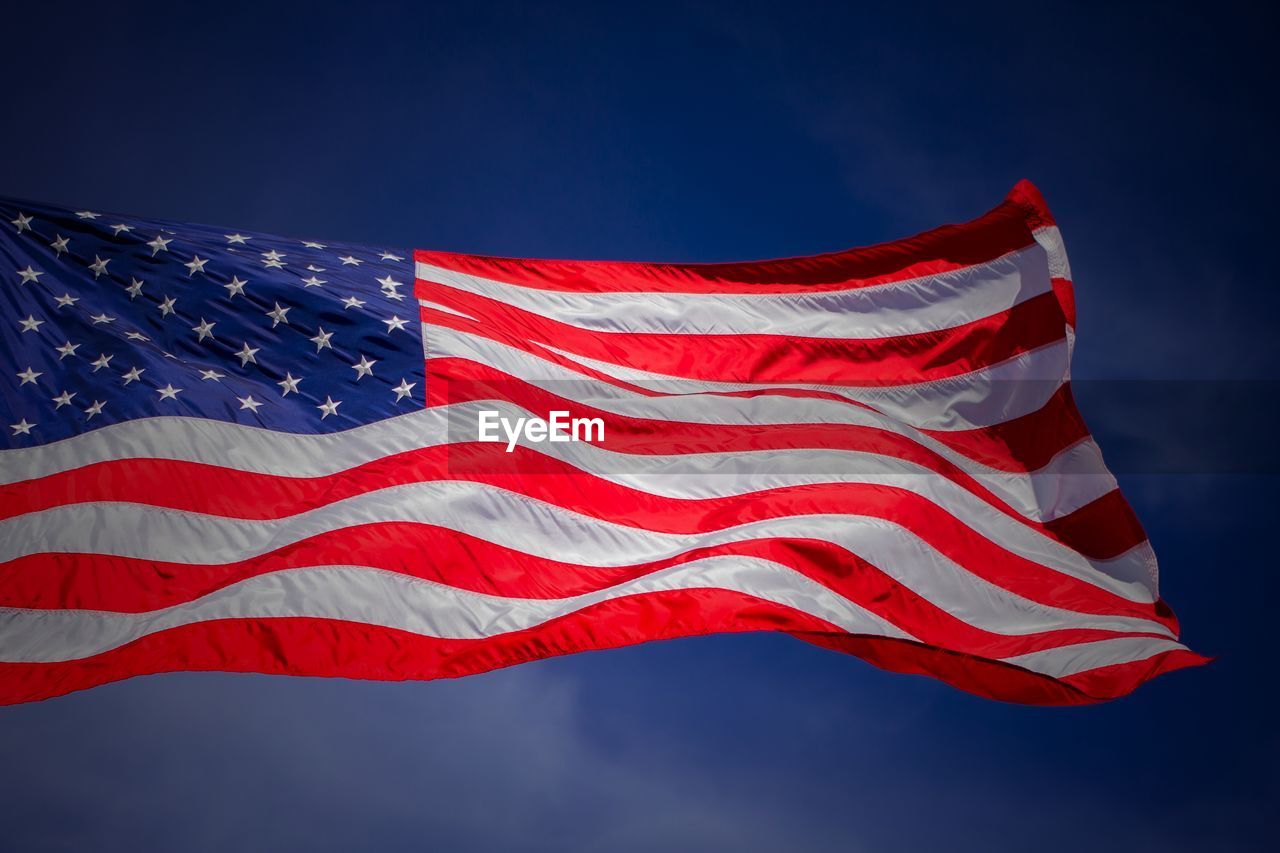 Low angle view of american flag waving against blue sky