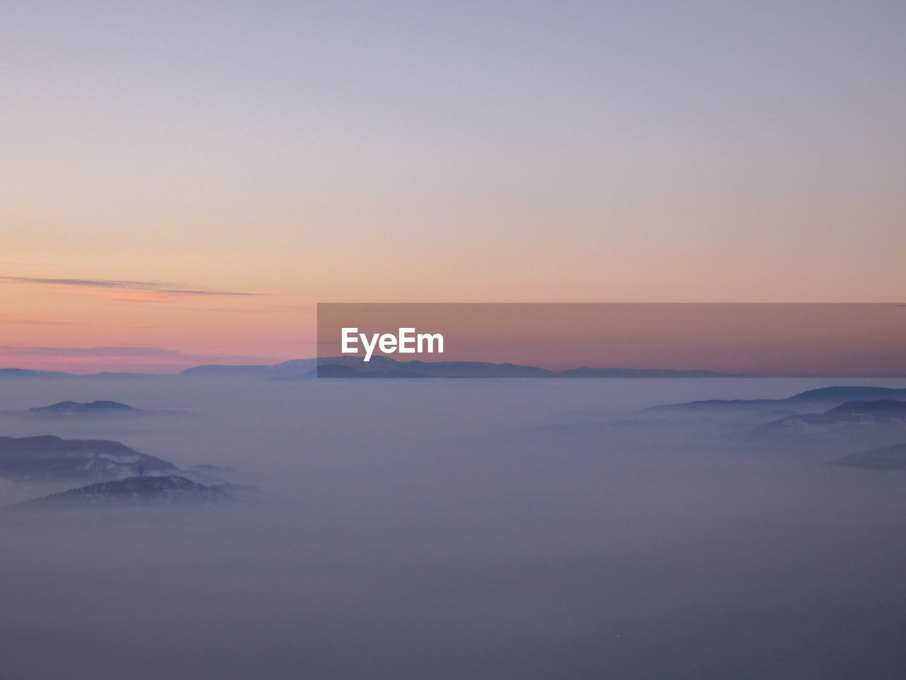 Scenic view of foggy landscape against sky during sunset