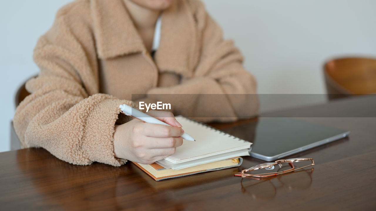 midsection of woman reading book while sitting on table