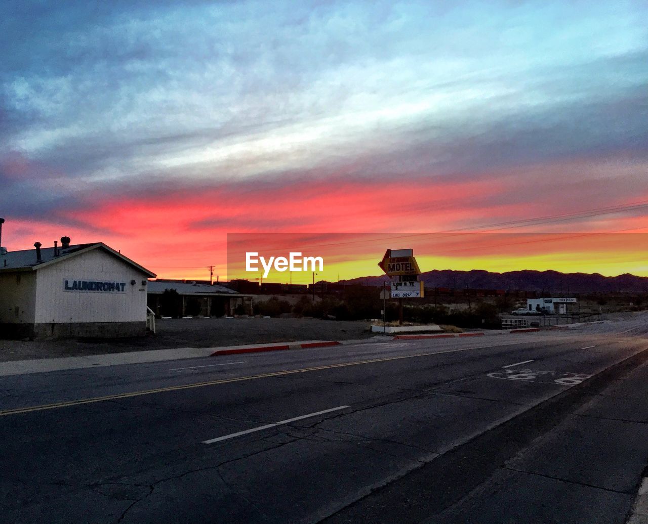 Road in town by field against sky during sunset