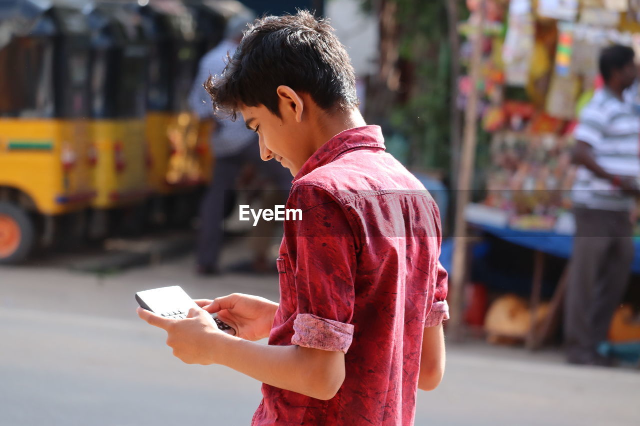 Young boy or man holding mobile phone while standing on street,travel and adventure concept