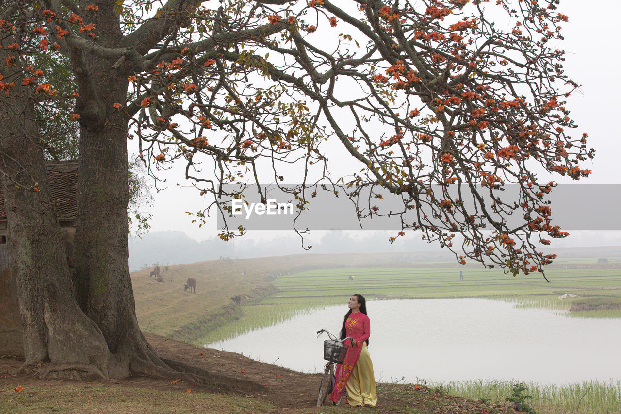 plant, tree, nature, flower, adult, one person, landscape, beauty in nature, environment, women, water, tranquility, sky, full length, fog, clothing, land, scenics - nature, lake, rural scene, leaf, outdoors, autumn, morning, tranquil scene, red, day, rear view, religion, travel, leisure activity, rural area, traditional clothing, tradition, lifestyles, men, grass, branch, travel destinations, standing, non-urban scene, field, walking, holiday