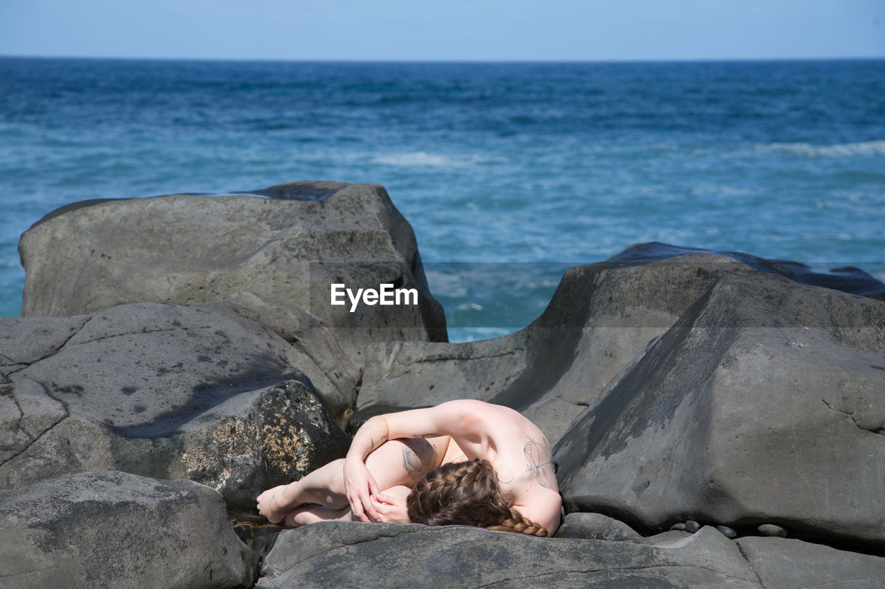 Naked woman lying on rocky shore