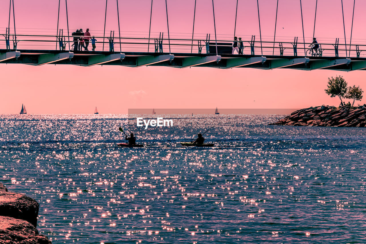 Silhouette people on bridge over sea against sky during sunset