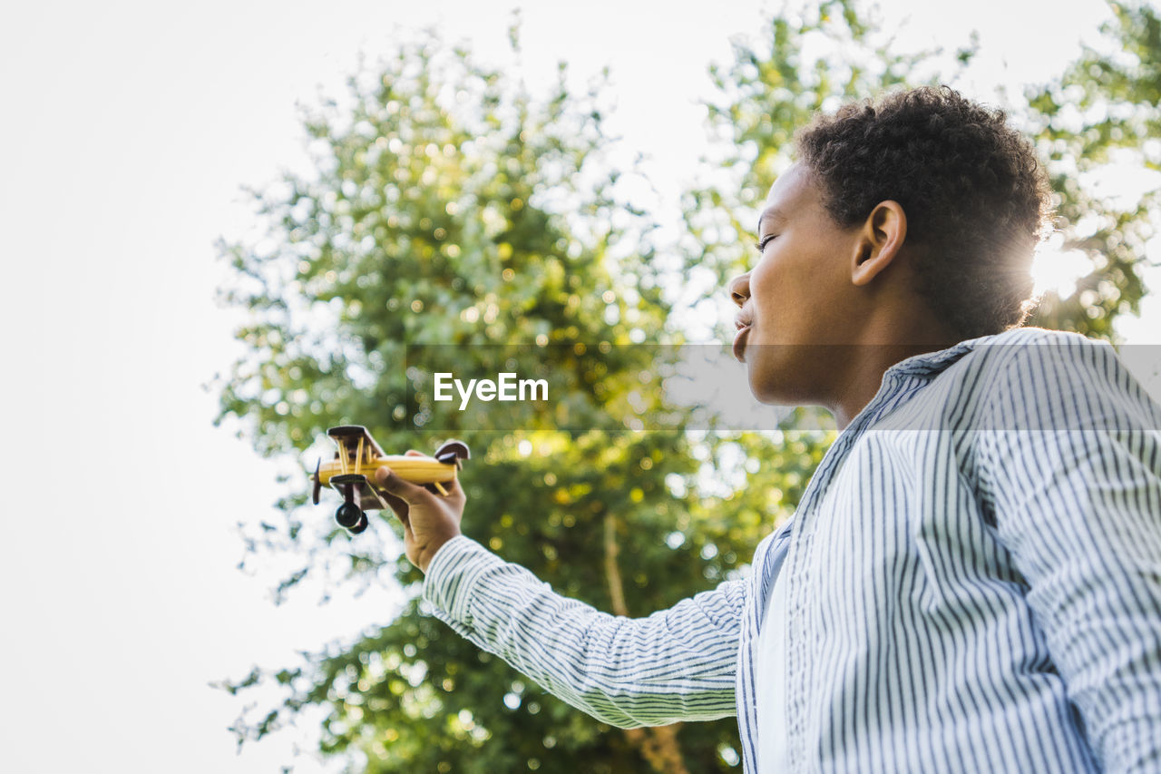 Young woman holding violin while standing against sky