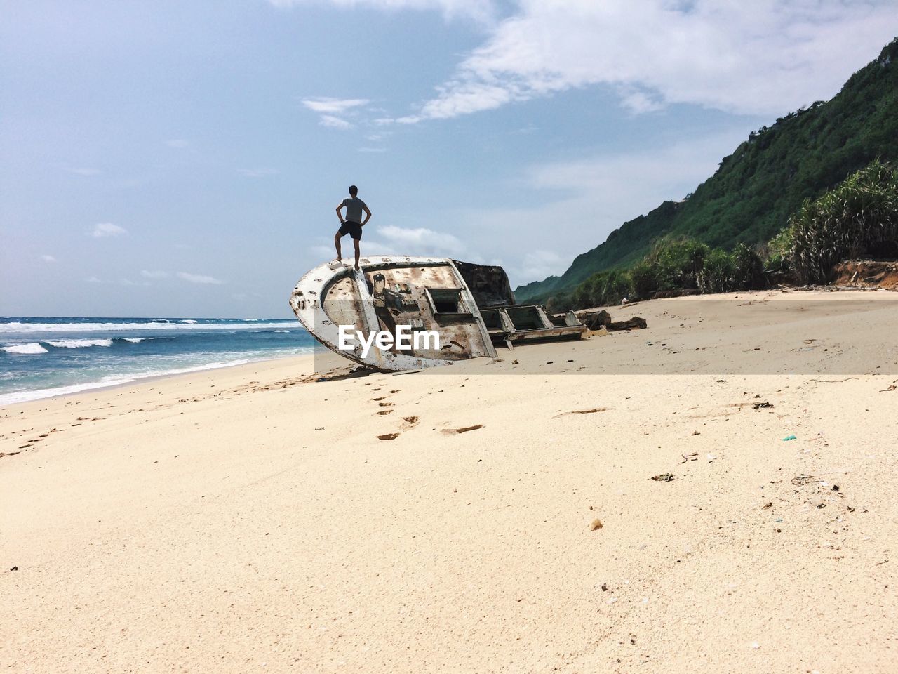 Man standing on shipwreck at beach against sky