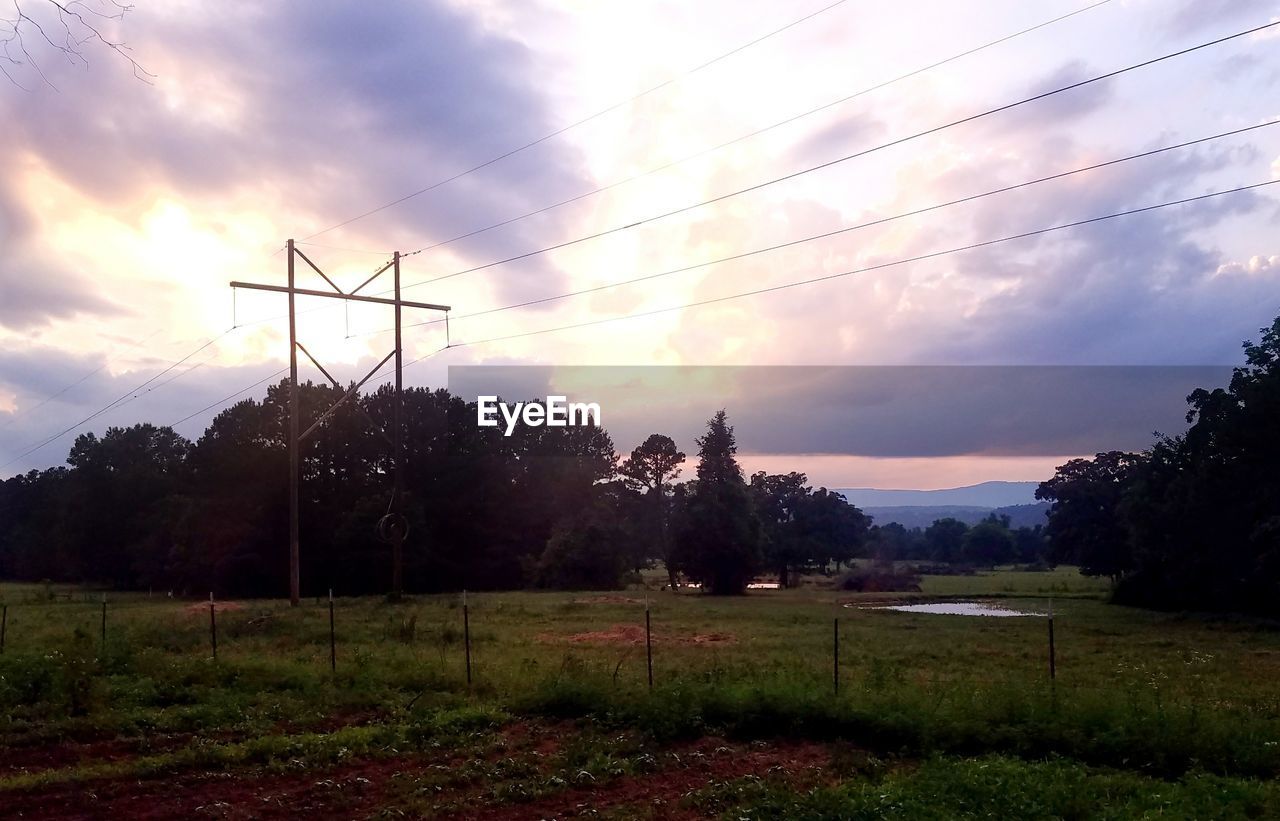 ELECTRICITY PYLONS ON FIELD AGAINST SKY DURING SUNSET