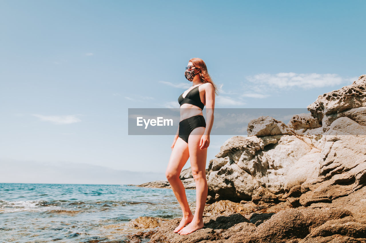 Full length of woman standing on rock by sea against sky