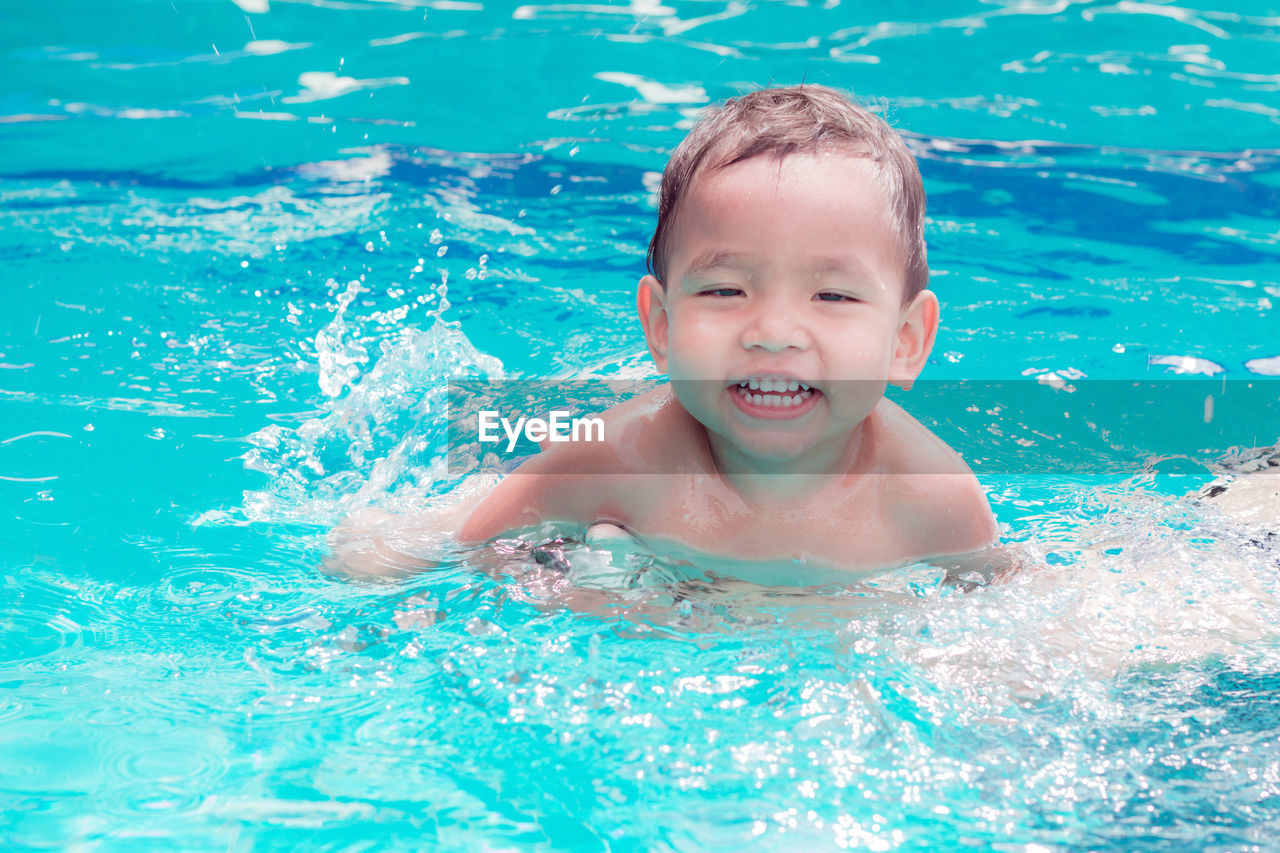 PORTRAIT OF BOY SMILING SWIMMING IN POOL