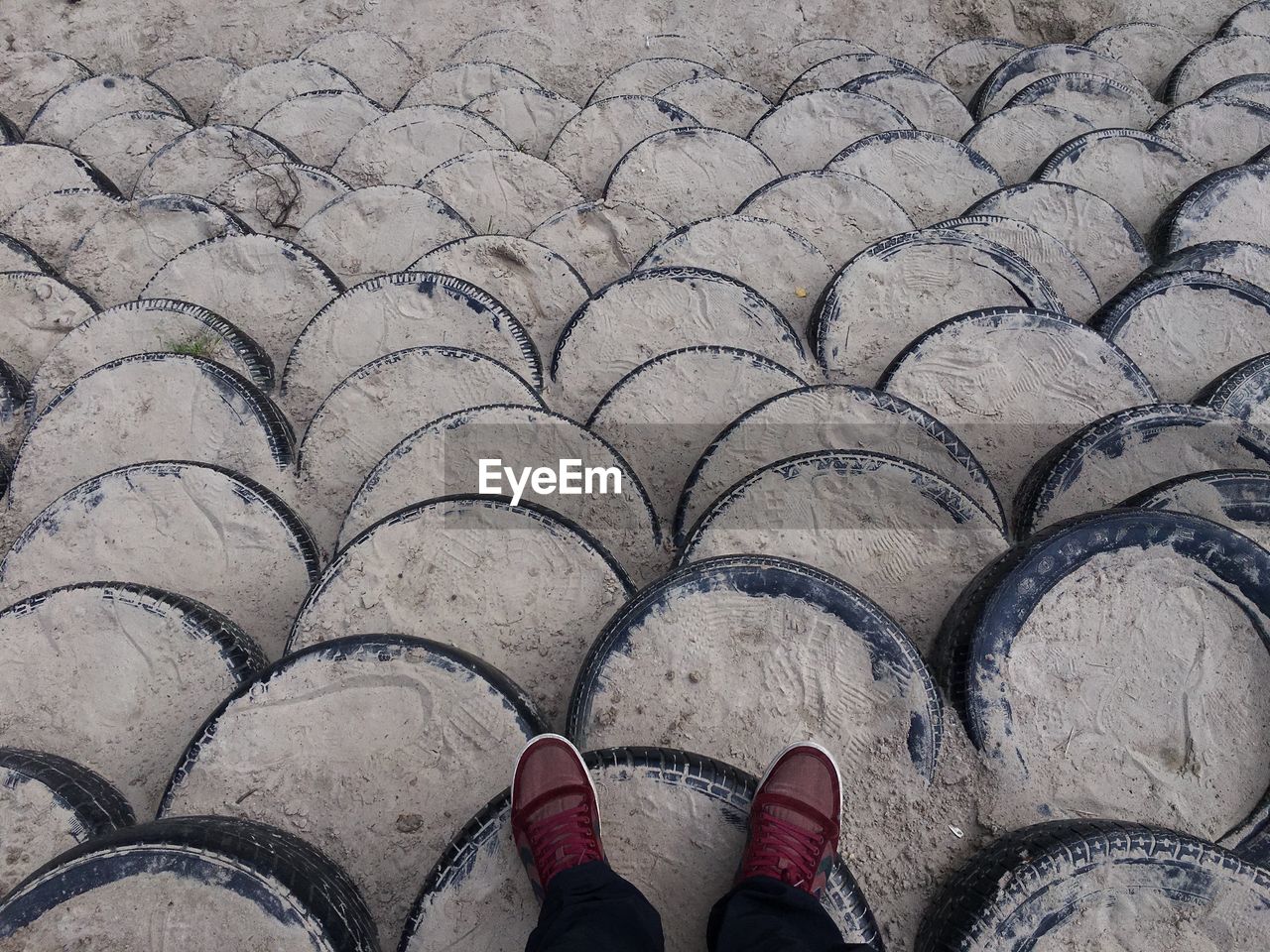 Low section of man standing on sand covered tires