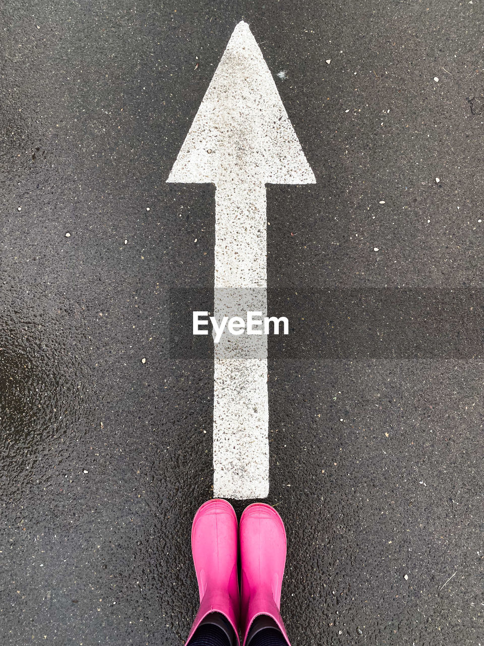 road, sign, one person, symbol, low section, arrow symbol, human leg, shoe, city, street, high angle view, personal perspective, standing, pink, asphalt, marking, red, transportation, day, road marking, guidance, directional sign, communication, white, black, outdoors, limb, human limb, number