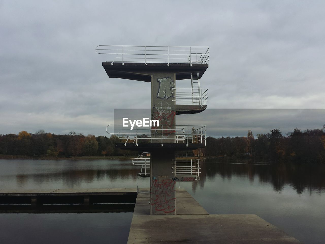Diving tower at lake against cloudy sky