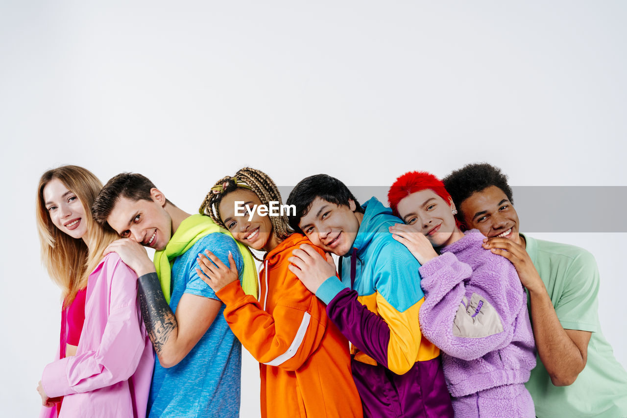 Group of young people in colorful clothes with hands on shoulder standing on white background