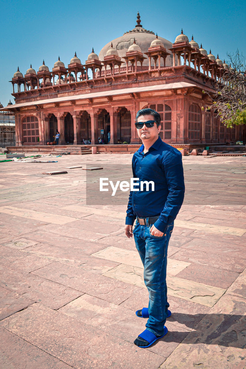 FULL LENGTH PORTRAIT OF YOUNG MAN STANDING AGAINST HISTORICAL BUILDING