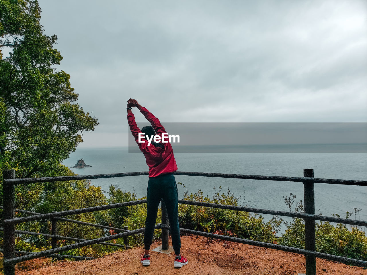 REAR VIEW OF WOMAN STANDING ON RAILING AGAINST SEA