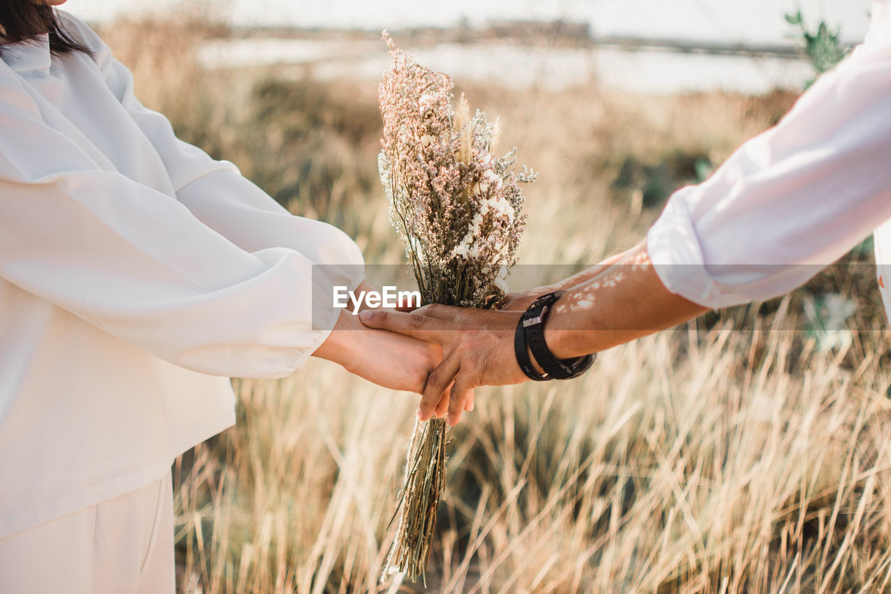 Wedding couple holding flowers while standing on grassy field