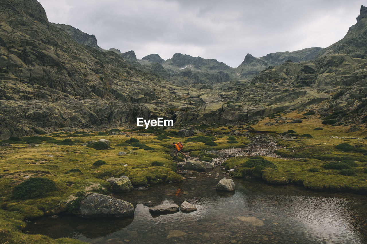 A young man jumps over a creek while hiking in sierra de gredos, spain