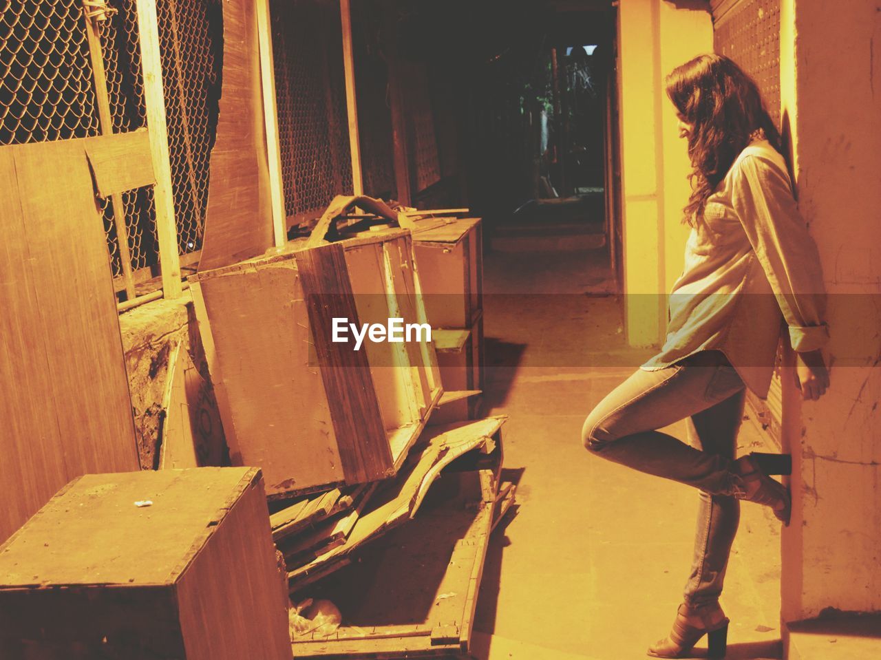 Full length of woman leaning on wall by abandoned furniture at night