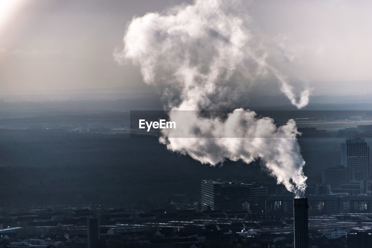 Chimney in city emitting smoke against sky