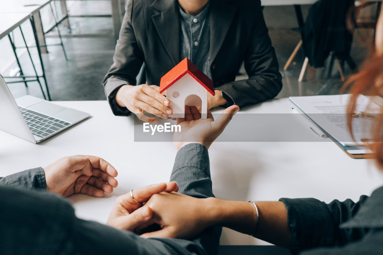 Midsection of man and real estate agent holding model home