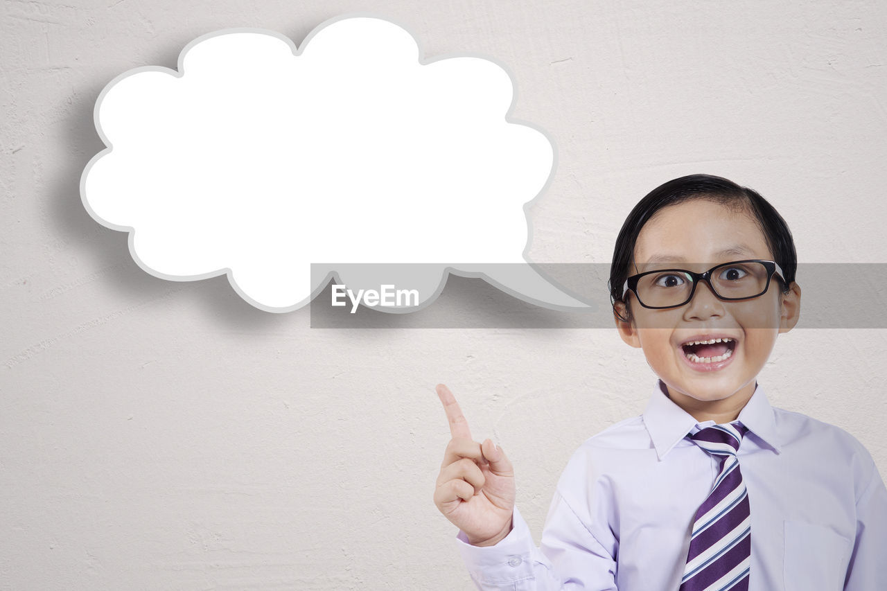 Portrait of happy boy with thought bubble standing against white background