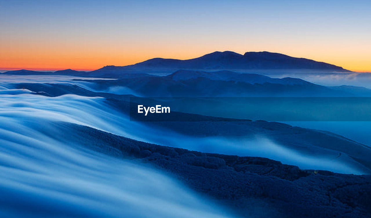 Scenic view of mountains against blue sky at sunset