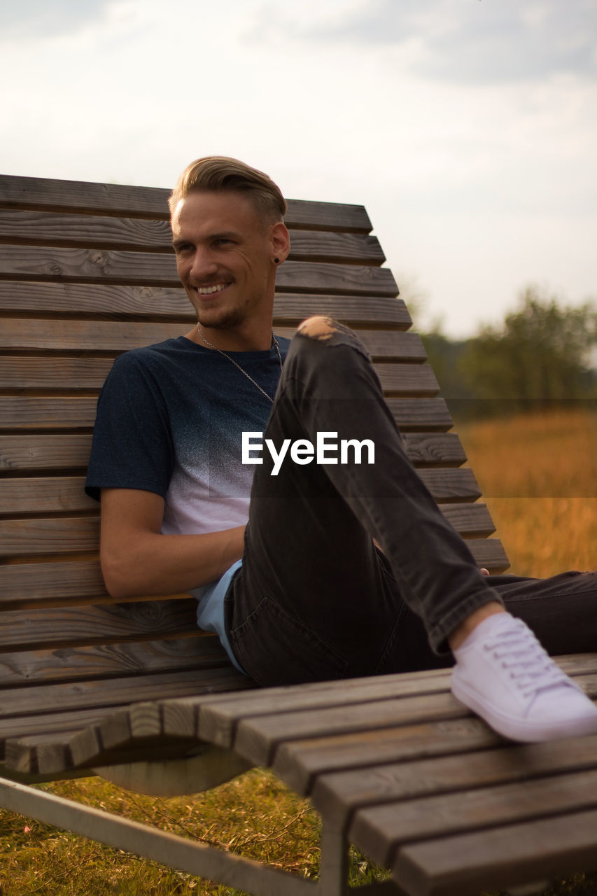 Man sitting on wooden lounge chair at field