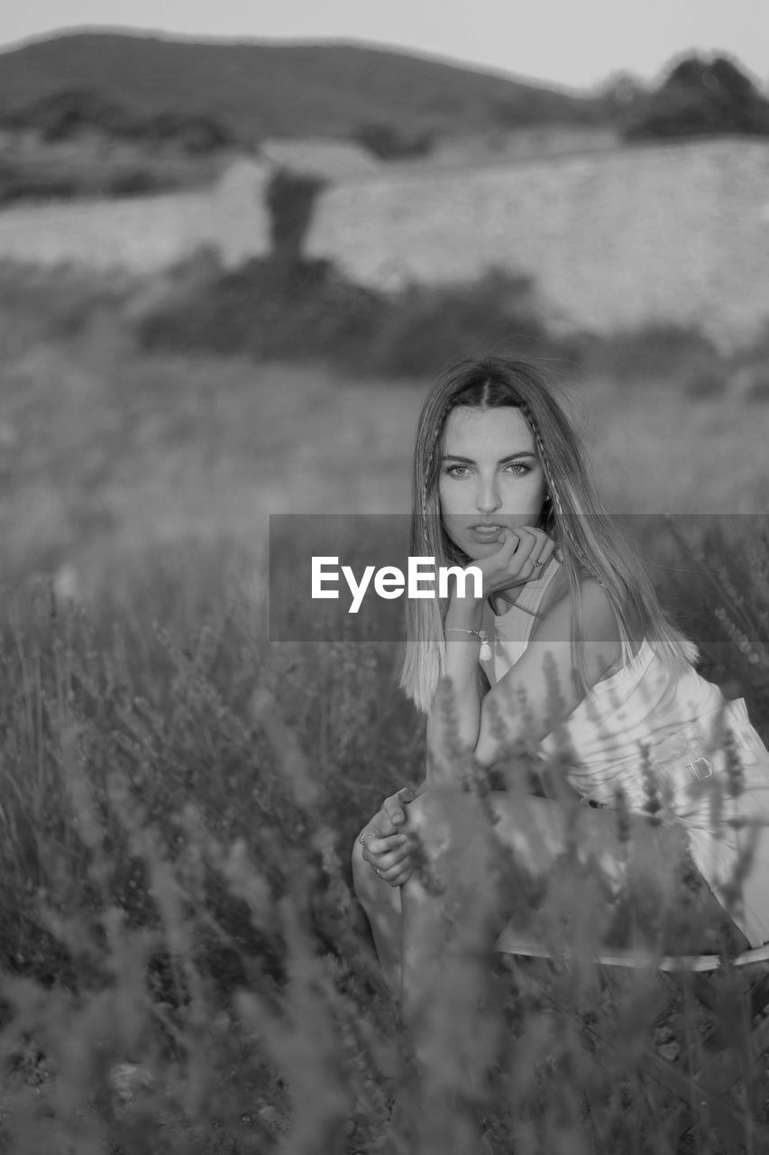 Beautiful young woman posing seated and looking straight ahead in a field of lavender blossoms