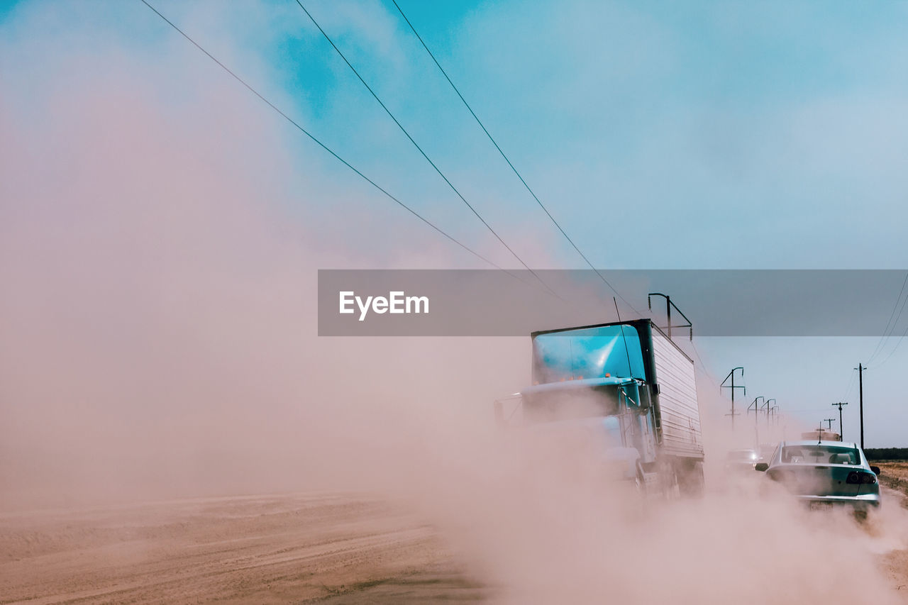 Vehicles on dirt road against sky