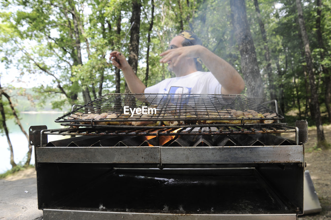 Man preparing meat on barbecue grill in forest