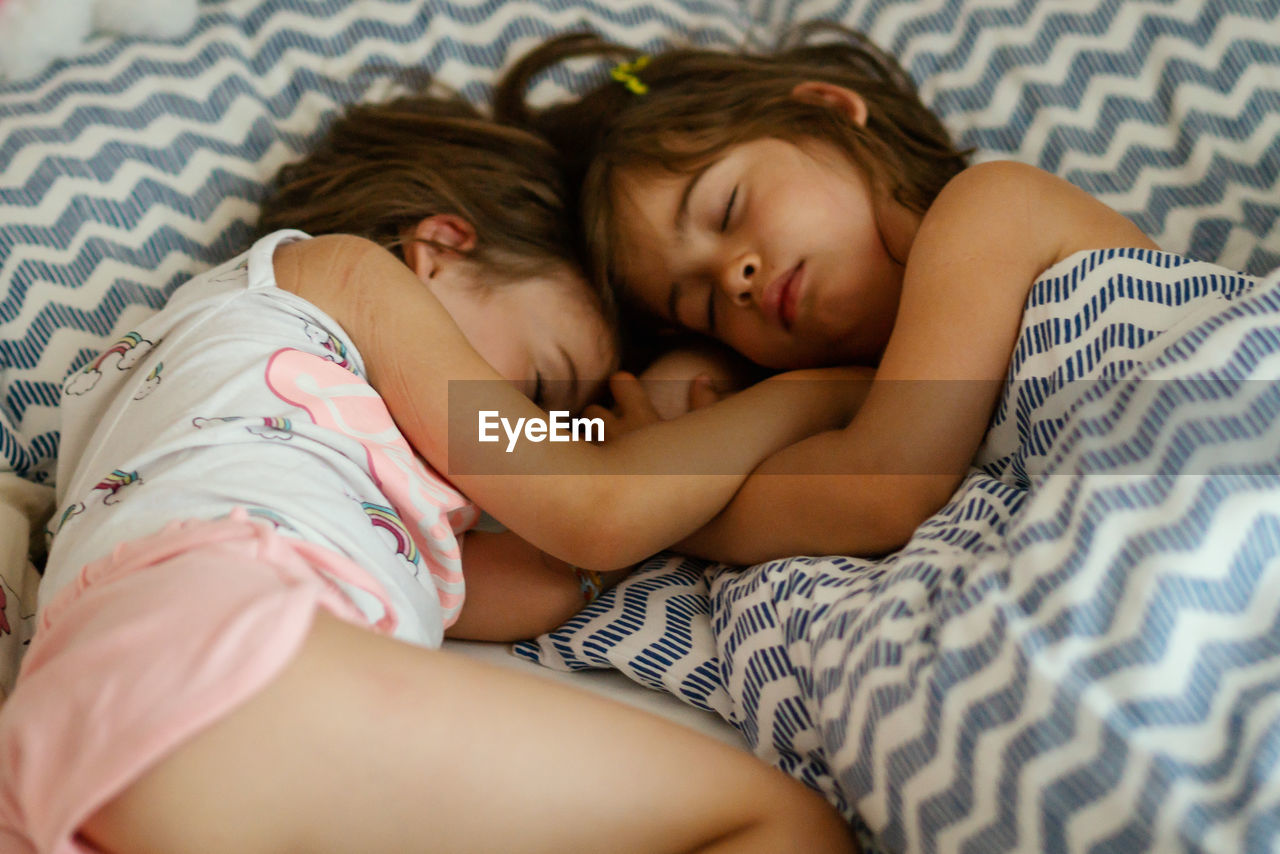 High angle view of sisters sleeping on bed