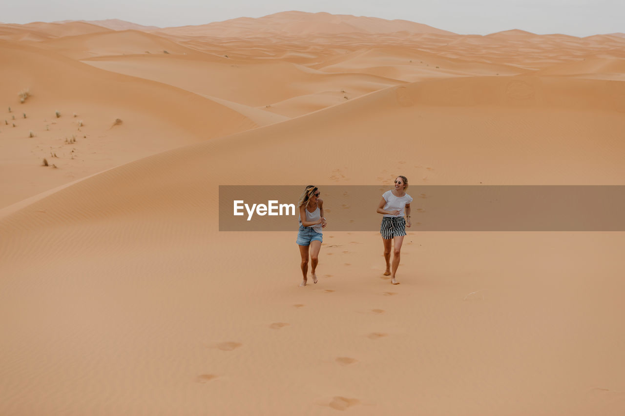 REAR VIEW OF PEOPLE WALKING ON SAND DUNE