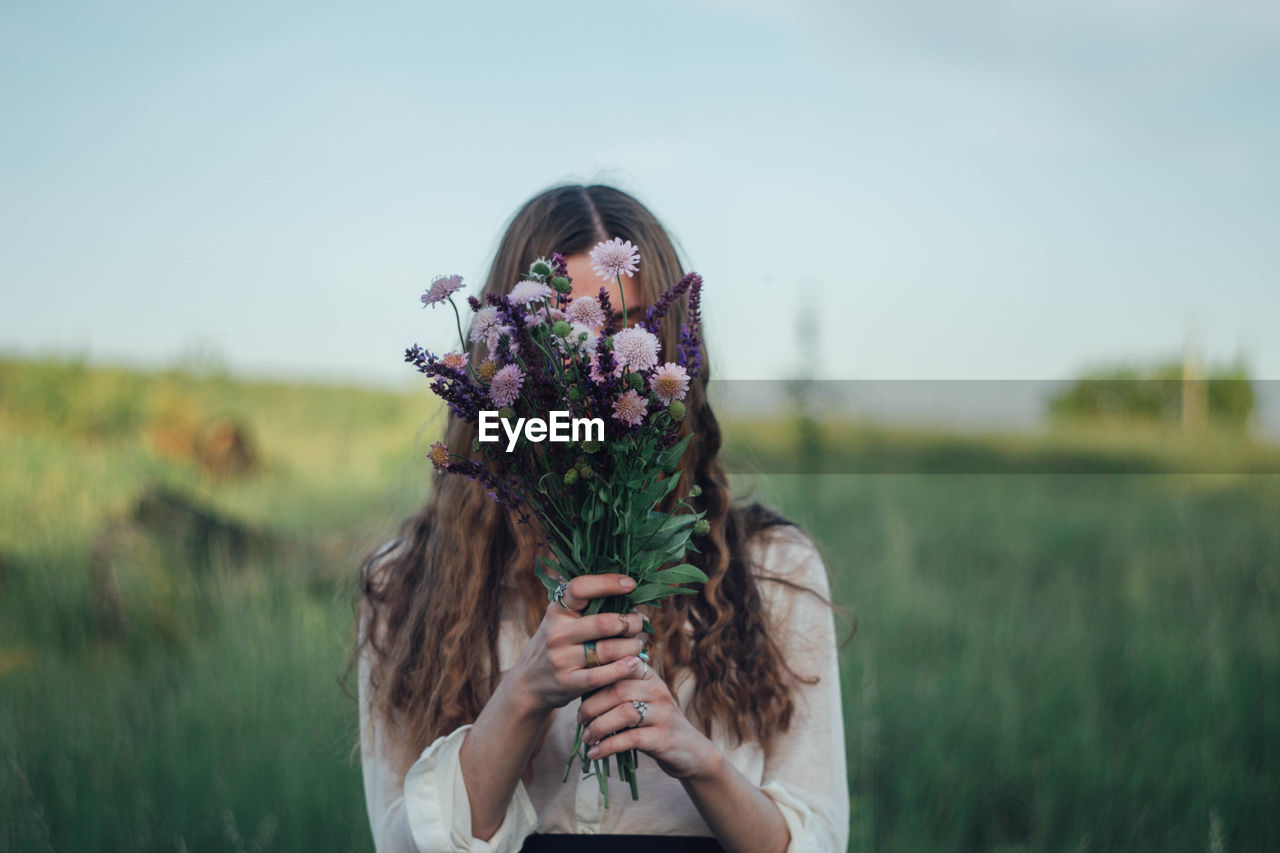 Young woman covering face with flowers while standing on land