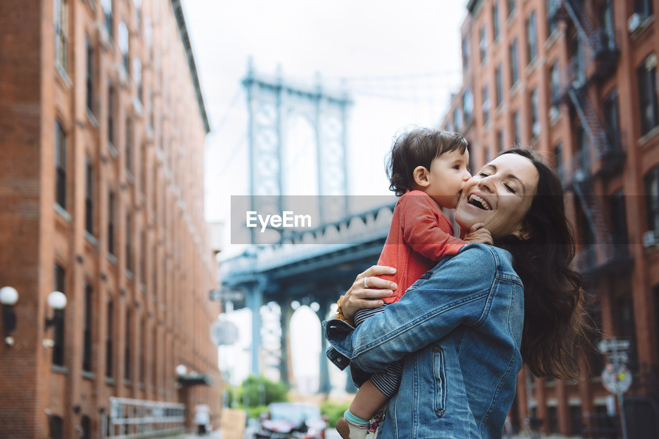 Usa, new york, new york city, baby kissing mother in brooklyn with manhattan bridge in the background