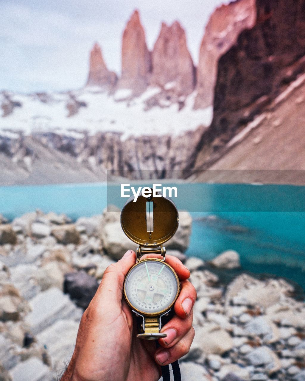 Close-up of man holding navigational compass against lake and mountain