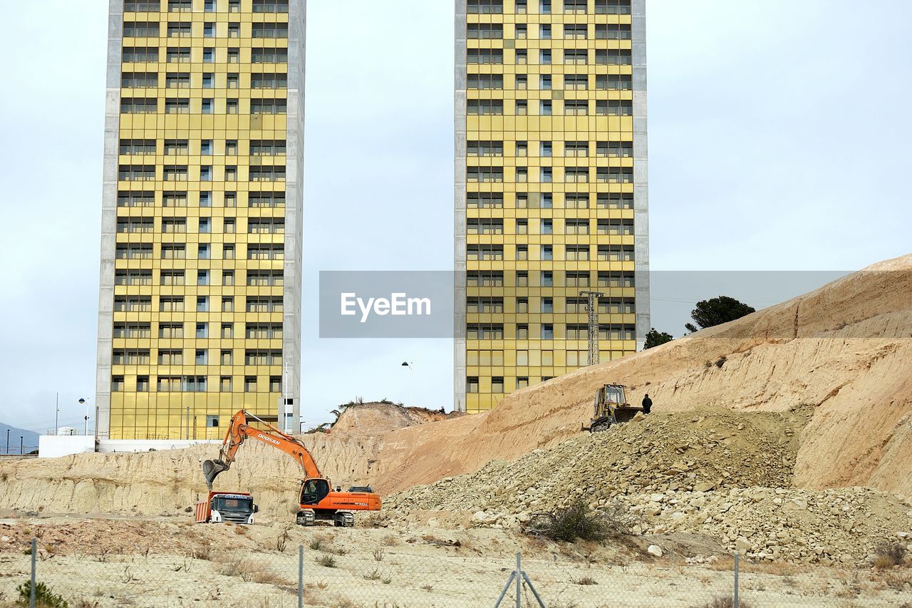 Bulldozer at construction site by modern buildings against sky