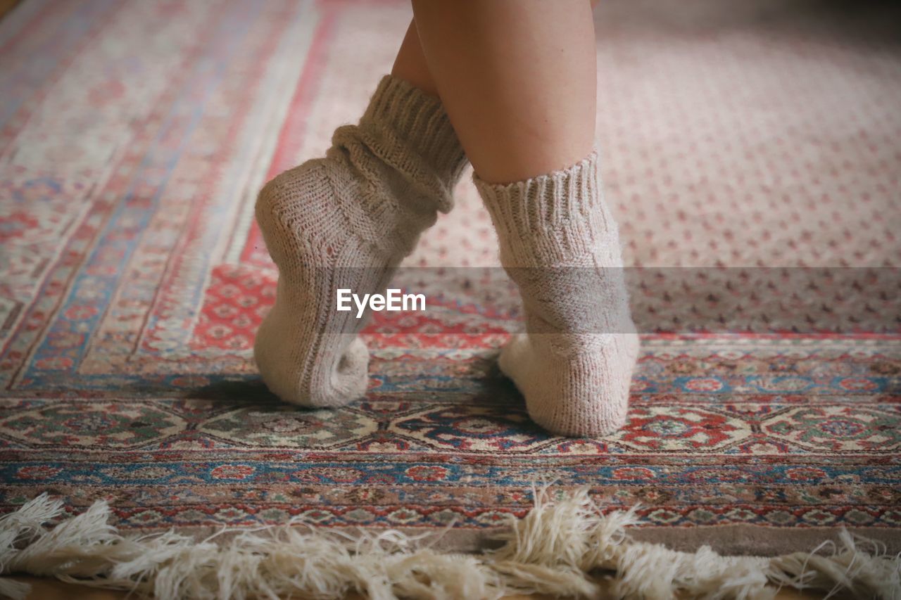 Low section of woman wearing socks standing on carpet at home