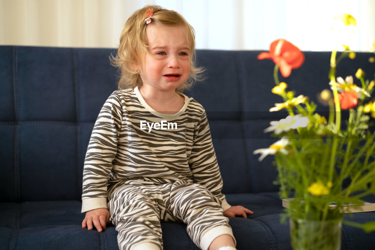 Cute girl crying while sitting on sofa at home