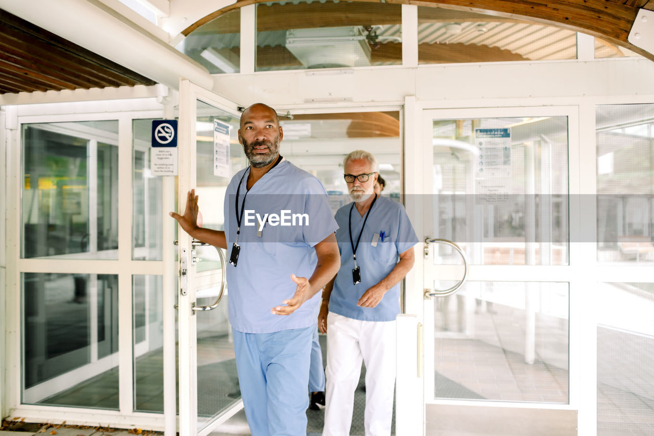 Mature nurse talking to senior colleague while holding hospital door