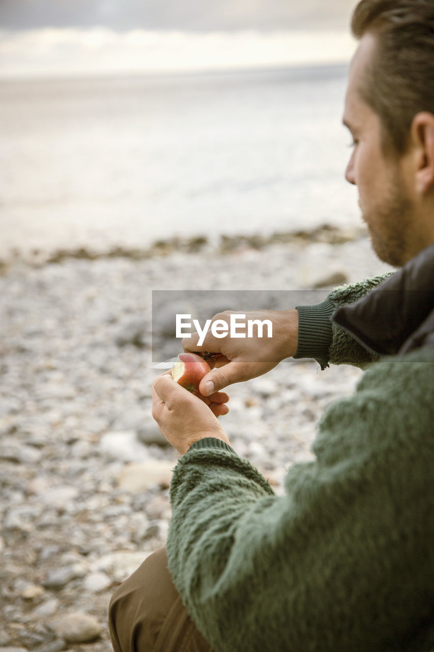 Cropped image of man cutting apple at beach