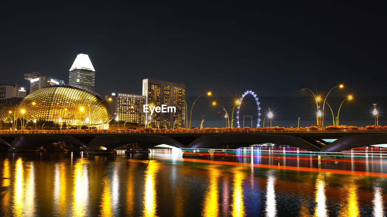 ILLUMINATED BRIDGE OVER RIVER AGAINST BUILDINGS AT NIGHT