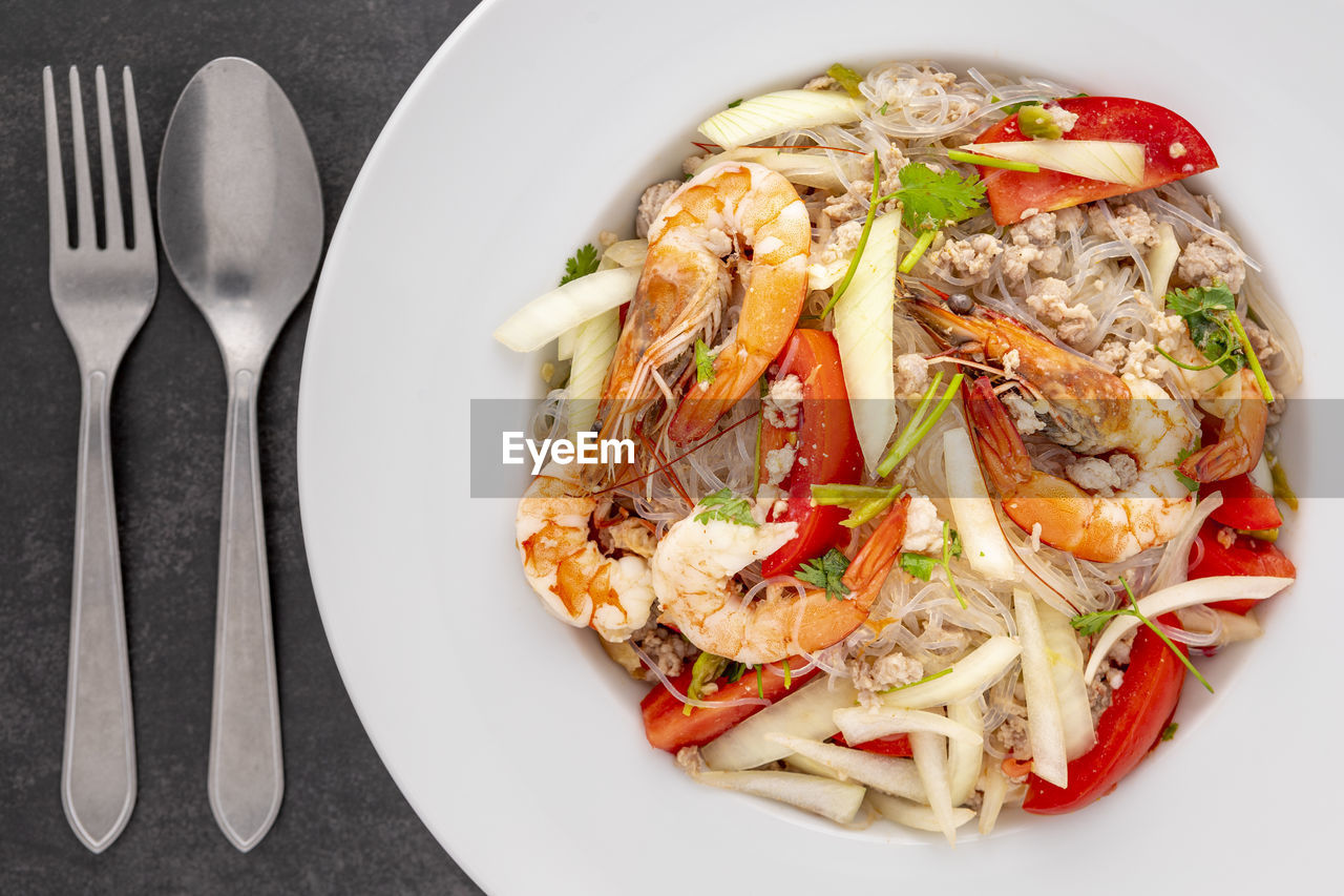 Yum woon sen, thai food, thai glass noodle salad in white ceramic plate beside spoon and fork