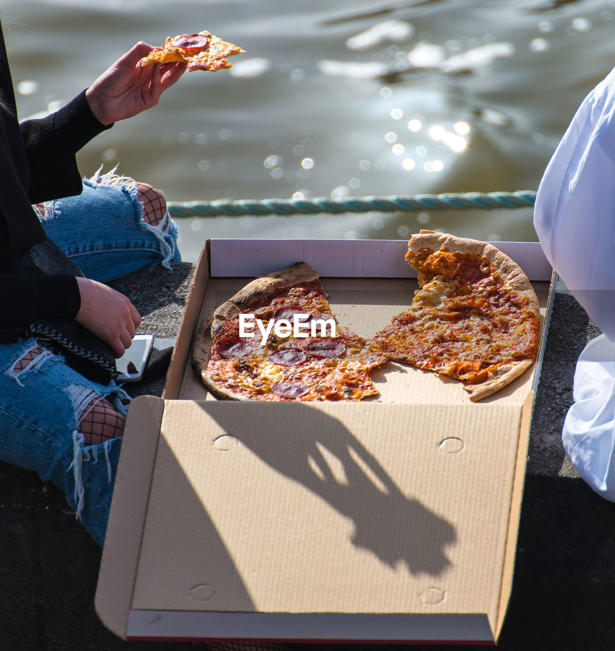 Close-up of people eating pizza by water