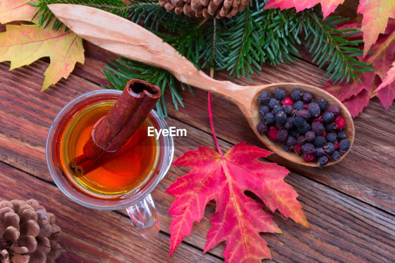 Tea with cinnamon and lemon, autumn leaves of maple, hawthorn berries in a wooden spoon on a table