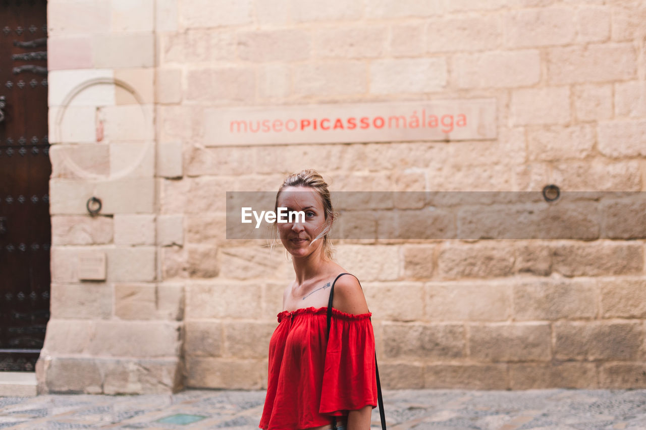 PORTRAIT OF A SMILING YOUNG WOMAN STANDING OUTDOORS