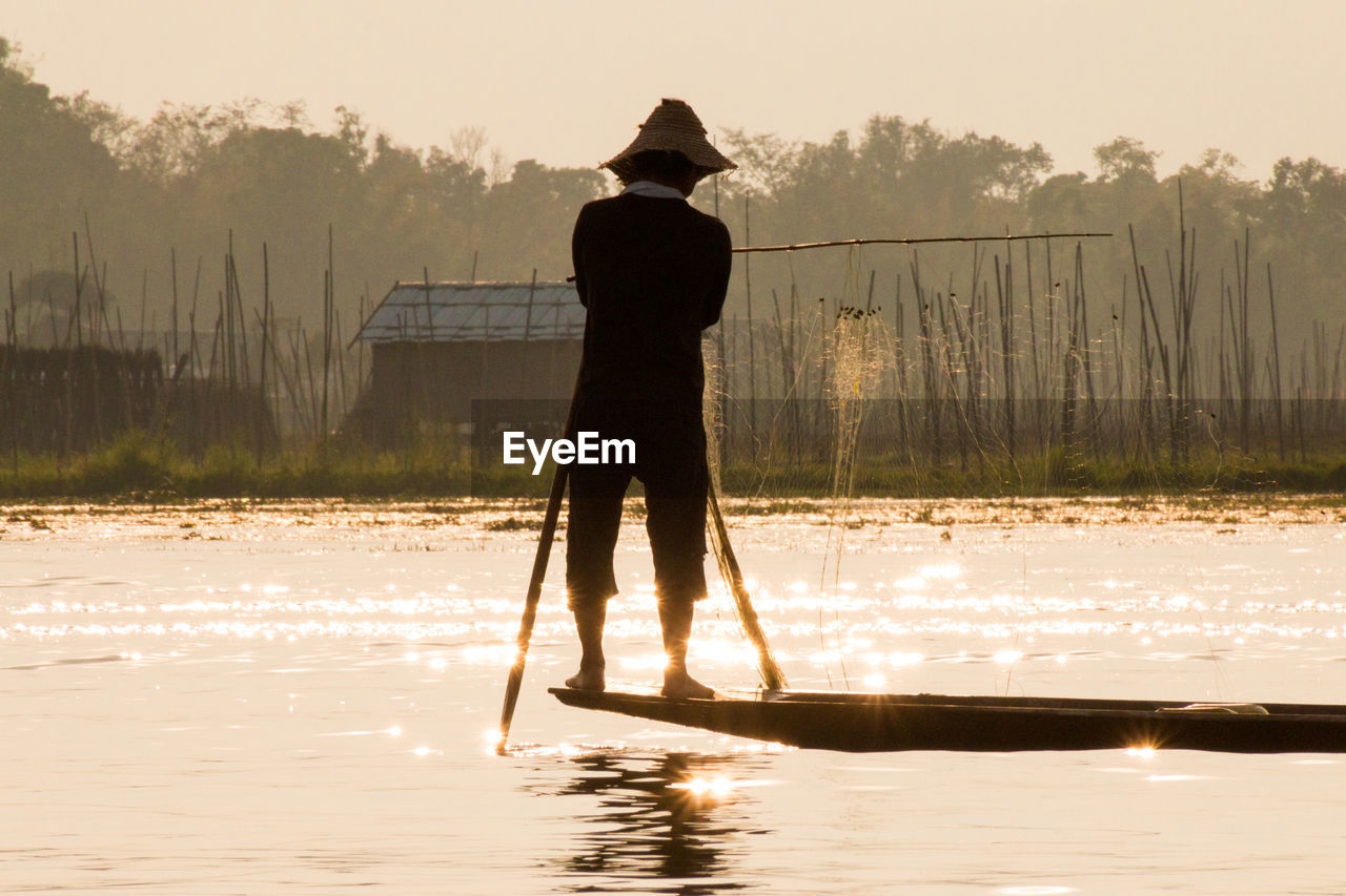 REAR VIEW OF MAN STANDING IN LAKE AGAINST SKY