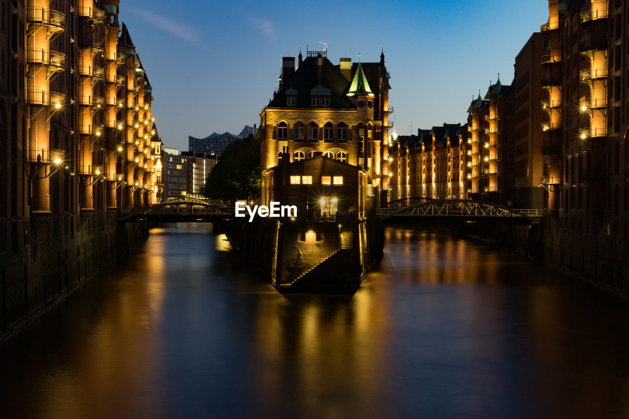 Bridge over canal amidst buildings in city at night