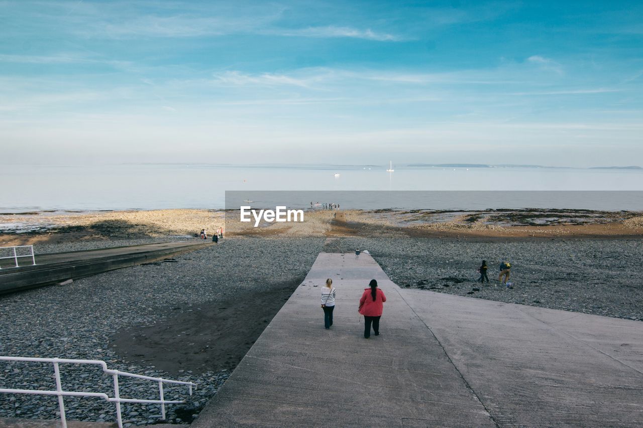 Rear view of women standing on shore at beach against sky