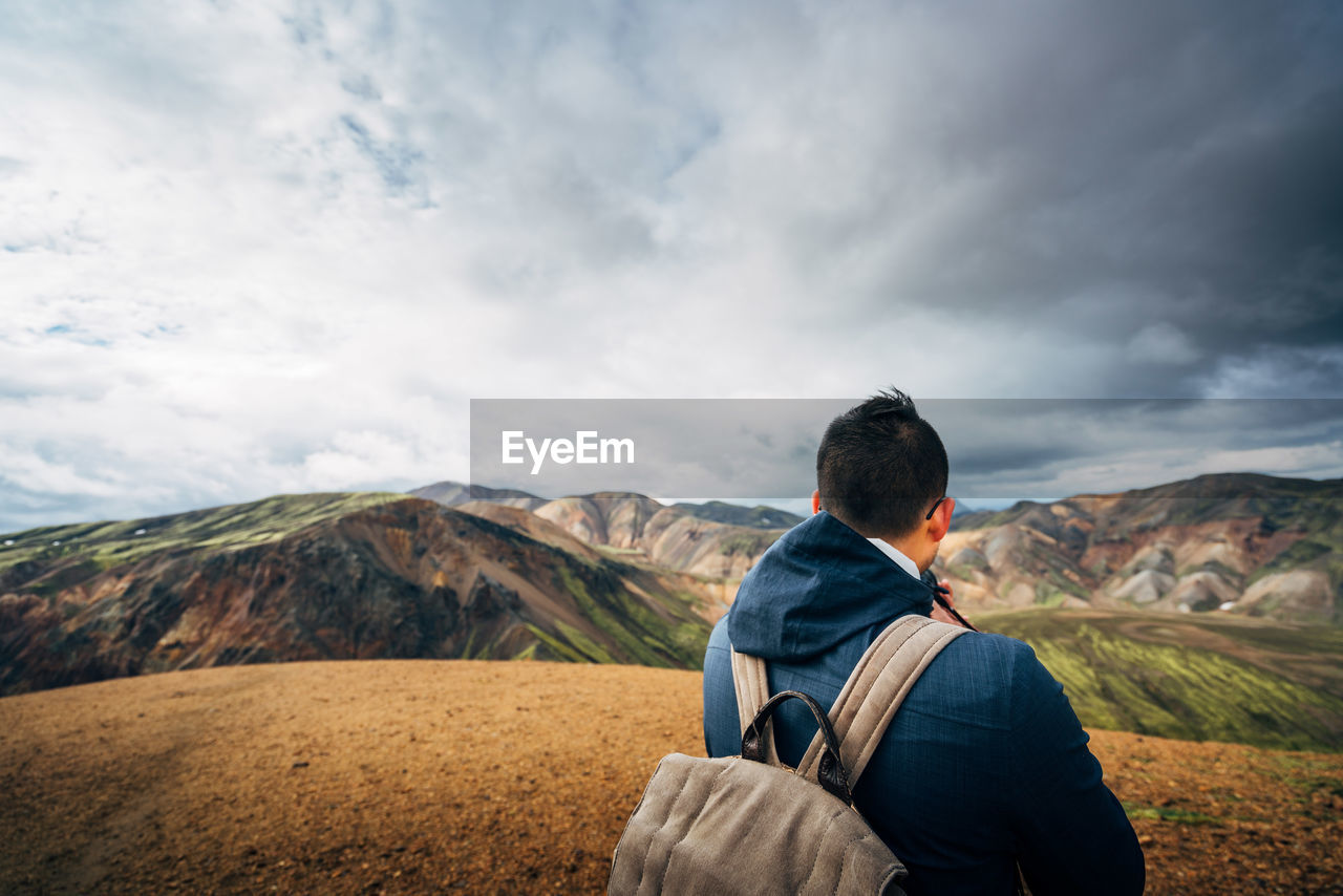 Rear view of hiker looking at mountains against cloudy sky